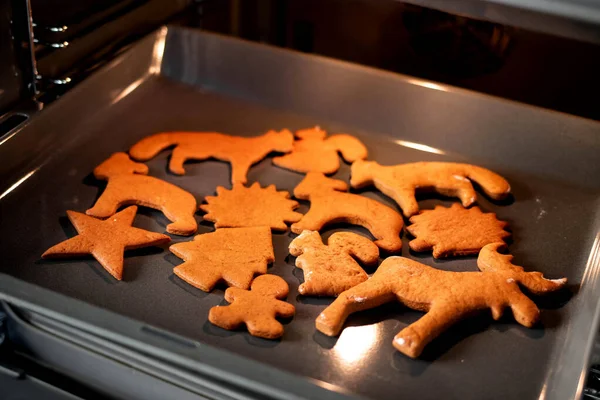 Close up Christmas gingerbread on a baking sheet in open modern oven in a bright kitchen. Christmas cookies in the oven - warm light, festive atmosphere. Concept of winter, Christmas, and New Year.