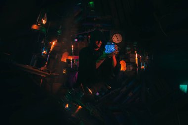 Simyacı sihirbaz elinde iksir olan bir şişe tutuyor. Büyücü karanlık laboratuvarda büyücüdür.