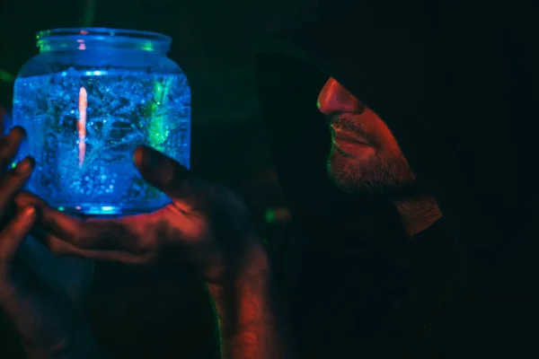 Alchemist Zauberer mit einem Fläschchen Zaubertrank in der Hand in einer schrecklichen Werkstatt. Zauberer in einem Halloween — Stockfoto