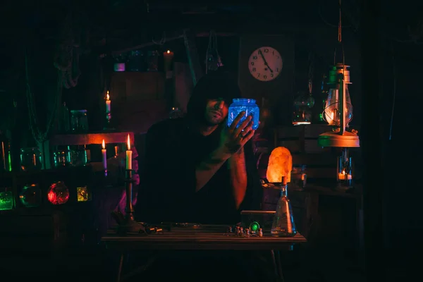 Witcher alchemist makes a secret potion in gloomy laboratory workshop. Magician sorcerer in Halloween costume — Stock Photo, Image