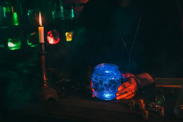 Hands of magician alchemist scientist with a flask with a magic potion at table — Stock Photo, Image