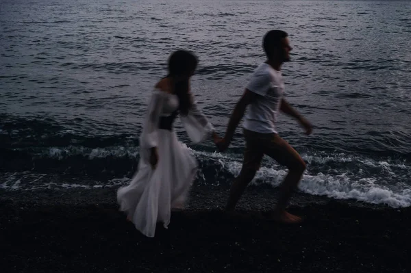 Pareja enamorada cogida de la mano corriendo por la playa junto al mar — Foto de Stock