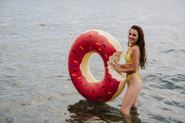 Mujer delgada con un cuerpo sexy en un traje de baño con un círculo inflable en sus manos está descansando en el mar — Foto de Stock