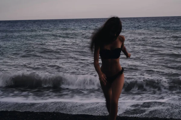 Glückliches Mädchen im Badeanzug läuft an einem Sommerabend fröhlich an den Meereswellen am Strand entlang — Stockfoto