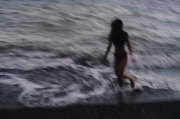 Šťastná dívka v plavkách šťastně běží podél moře vlny na pláži v letním večeru — Stock fotografie