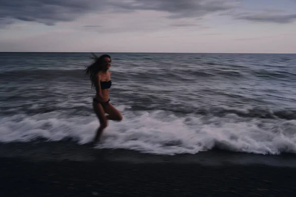 Feliz joven en un traje de baño se ejecuta en las olas del mar en la playa — Foto de Stock