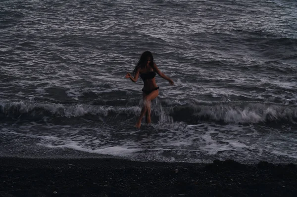 Счастливая девушка в купальнике счастливо бегает по морским волнам на пляже летним вечером — стоковое фото