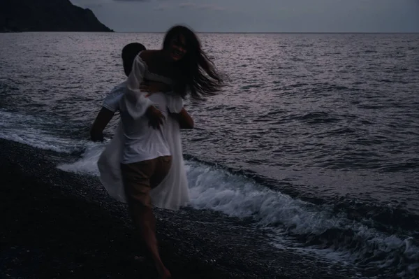 Влюбленный мужчина таскает свою девушку на спине по берегу моря — стоковое фото