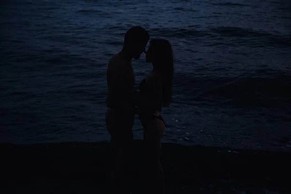 Голубая пара влюблена девушка и мужчина обнимает и целует в воде в море на пляже в летнюю ночь — стоковое фото