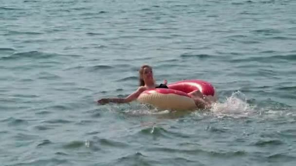 Jonge vrouw in een badpak zwemt op een opblaasbare cirkel in de zee in de zomer — Stockvideo