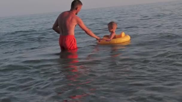 Homme papa enseigne garçon fils à nager sur un cercle gonflable dans la mer en été — Video