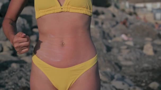 Λεπτή κοπέλα με μαυρισμένο δέρμα απλώνει αντηλιακό στην κοιλιά της το καλοκαίρι στην παραλία — Αρχείο Βίντεο