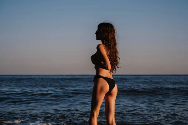 Young brunette girl topless with a sexy ass on the beach sunbathing by the sea — Stockfoto