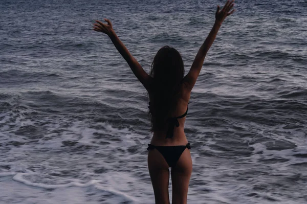 Fille lève les mains joyeusement sur la plage sur le bord de la mer avec des vagues en été — Photo