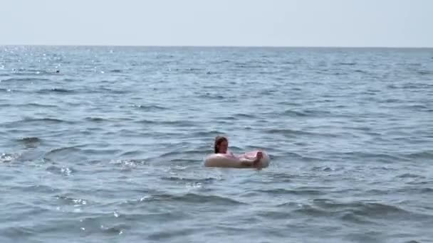 Κορίτσι με μαγιό κολυμπάει σε έναν φουσκωτό κύκλο στη θάλασσα — Αρχείο Βίντεο