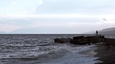 silhouette of a fisherman with a fishing rod fishing on a dramatic sea with waves on the beach in the evening