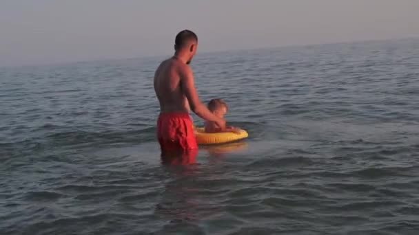 Man dad teaches boy son to swim on an inflatable circle in the sea in summer — Stock Video
