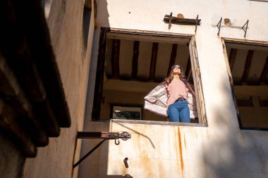 Güneşli bir sonbahar sabahında harap olmuş bir odanın penceresinden sarkan genç bir kadın.