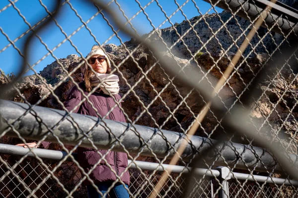 Молода жінка з вовняним капелюхом і морським пальто позує за ґратами — стокове фото