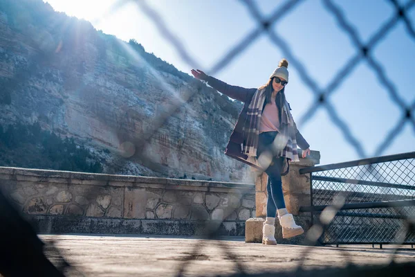 Молода жінка стоїть з витягнутими руками в пальто і капелюсі за парканом на відкритому повітрі — стокове фото
