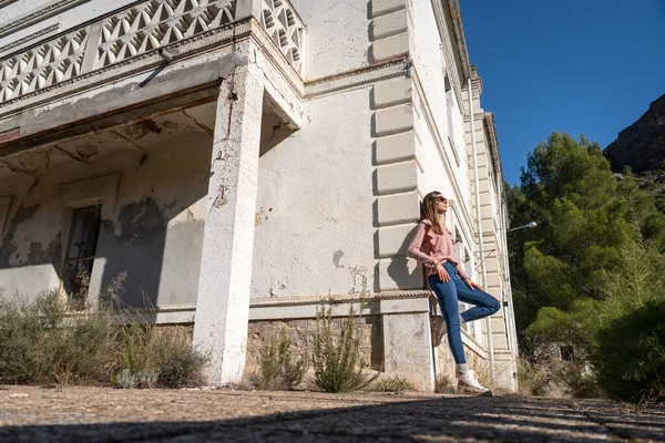 Молода жінка в джинсах спирається на білу стіну зруйнованого будинку — стокове фото