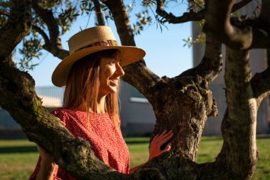 Young woman in red dress and hat in the middle of an olive tree