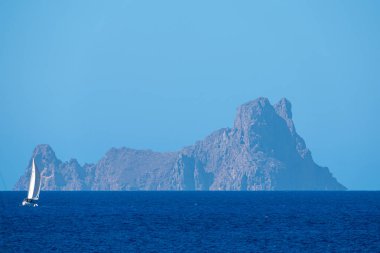 White sailboat sailing the sea with Es Vedra in the background clipart