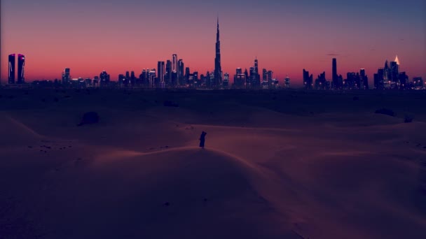 Wanita Arab mengenakan pakaian tradisional abaya berdiri di padang pasir dan terlihat di lampu kota Dubai pada malam hari. — Stok Video
