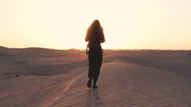 A woman walking towards the sunset in the desert. High quality 4k footage