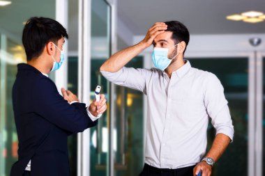 Otelin önünde yüz maskesi takan resepsiyonist, resepsiyonist, alnında vücut sıcaklığı kontrolü, Covid 19 ve koronavirüs enfeksiyonu koruma kavramı kullandıktan sonra onu otelde durdurdu.