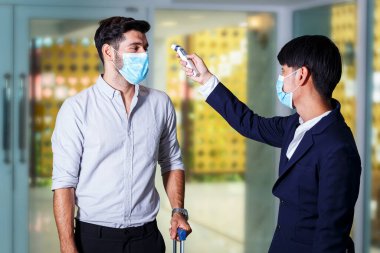 Otelin ön maskesinde bavul takan resepsiyonist ve misafir alnında vücut ısısı kontrolü, kovid 19 ve koronavirüs enfeksiyonu koruma kavramı kullanın.