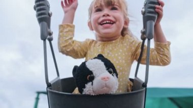 Küçük kız sallanırken kameraya gülümsüyor.