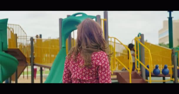 Мама на детской площадке улыбается и машет в камеру — стоковое видео