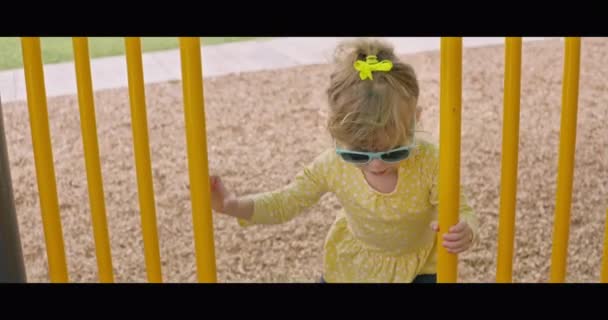 Όμορφο κοριτσάκι με γυαλιά ηλίου που παίζει σε παιδική χαρά — Αρχείο Βίντεο