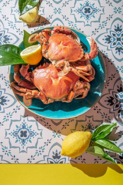 Mavi tabakta pişmiş yengeç, limon, masada gül şarabı, güneş ışığı göçü.