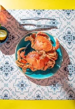 Mavi tabakta pişmiş yengeç, limon, masada gül şarabı, güneş ışığı göçü.
