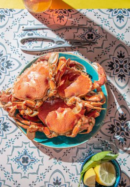Mavi tabakta pişmiş yengeç, limon, masada gül şarabı, güneş ışığı göçü.