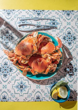 Mavi tabakta pişmiş yengeç, limon, masada gül şarabı, güneş ışığı göçü.