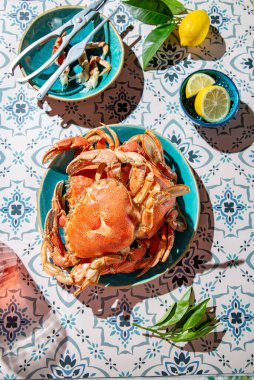 Mavi tabakta pişmiş yengeç, limon, masada gül şarabı, güneş ışığı göçü.