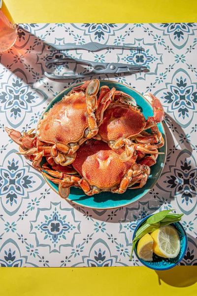 Mavi tabakta pişmiş yengeç, limon, masada gül şarabı, güneş ışığı göçü.