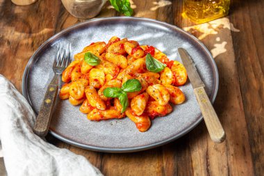 Domates soslu İtalyan Gnocchi ve ahşap arka planda fesleğen..