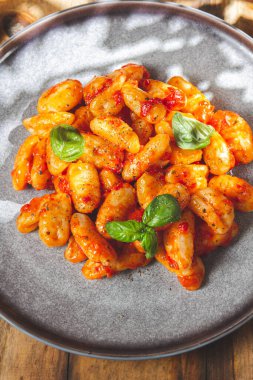 Domates soslu İtalyan patatesi Gnocchi ve ahşap arka planda taze fesleğen.