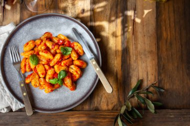 Domates soslu geleneksel İtalyan patatesi Gnocchi ve ahşap arka planda mavi tabakta taze fesleğen.