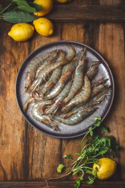 Gri tabakta çiğ karides, limon ve kişniş. Üst manzara, ahşap arkaplan.