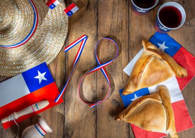 Chilean independence day concept. fiestas patrias. Tipical baked empanadas, wine or chicha, fat and play emboque. Decoration for 18 september party day, wooden background, top view. clipart