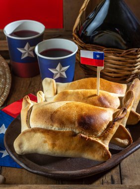 Şili 'nin bağımsızlık günü kavramı. fiestas patrias. Tipik pişmiş empanadas de pino, şarap ya da chicha, şapka ve emboque. 18 Eylül partisinde yemek ve içki, ahşap arka plan.