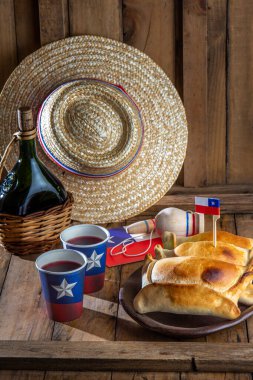 Şili 'nin bağımsızlık günü kavramı. fiestas patrias. Tipik pişmiş empanadas de pino, şarap ya da chicha, şapka ve emboque. 18 Eylül partisinde yemek ve içki, ahşap arka plan.