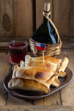 Şili 'nin bağımsızlık günü kavramı. fiestas patrias. Tipik pişmiş empanadas de pino, şarap ya da chicha, şapka ve emboque. 18 Eylül partisinde yemek ve içki, ahşap arka plan.