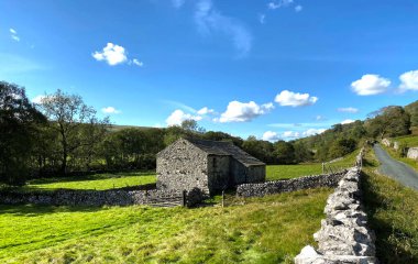 Hubberholme, Skipton, İngiltere 'nin yanındaki taştan bir ahır ve tarlaları olan kuru taştan bir duvarın üzerinden ikiye böleceğiz.