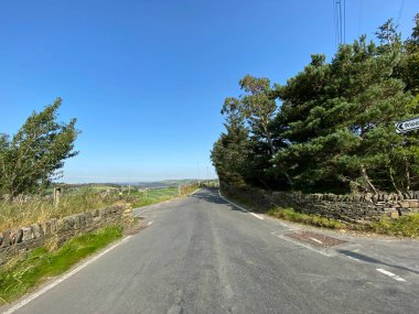 İngiltere 'nin Ripponden yakınlarındaki güneşli bir günde, kuru taş duvarlar, ağaçlar ve tarlalarla, Long Causeway yolu boyunca bakıyorum.